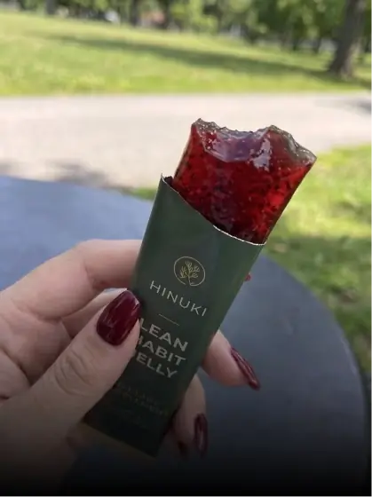 Person holding a bitten Hinuki Lean Habit Jelly stick outdoors